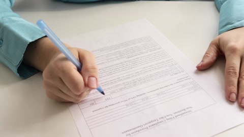 女性双手拿着钢笔在一张纸上写字，填写问卷