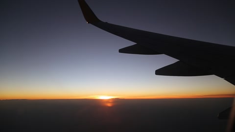 日出或日落时飞行的飞机机翼。