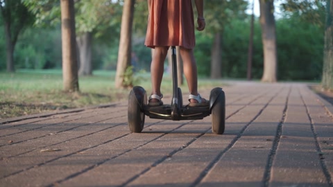 小女孩骑着吉罗滑板车在公园里行驶，镜头靠近，从背后拍摄