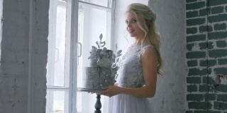 新娘站在窗前，手上拿着一份美丽的婚礼蛋糕