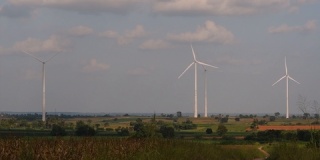 风力涡轮机高耸在农田上方，农民种植庄稼并照料