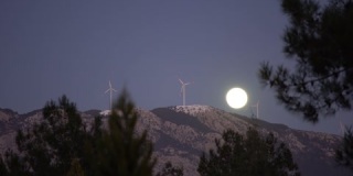风力涡轮机在晴朗的夜晚与山后的满月一起拍摄4K