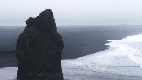 冰岛的黑沙滩，有巨石和悬崖，雾气笼罩，有鸟儿飞翔