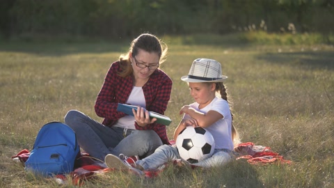 公园里快乐的家庭妈妈和女儿。妈妈给女儿读一本书视频素材模板下载