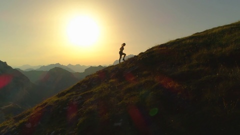 空中剪影：年轻女子在黄昏时分攀登山峰的轮廓
