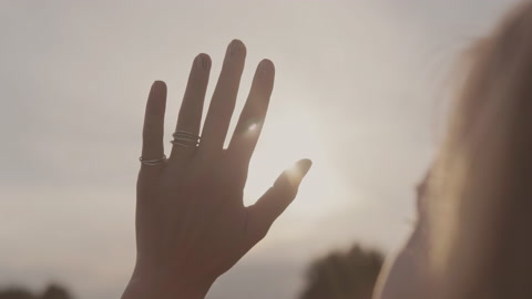 女人用手指着望日落的太阳手的近景