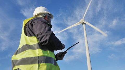 风力技术工人在风力涡轮发电厂背景下使用平板电脑