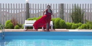 年轻女孩穿着长红裙子，慢动作跳入户外游泳池