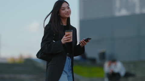 时尚的年轻女子在城市中走路，用手机打电话，拿着咖啡