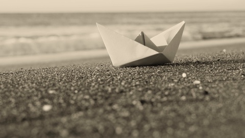 可爱的小纸船站在阳光明媚的夏日海滩上的沙滩上
