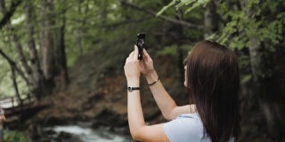 游客女孩使用手机拍照，小瀑布顺着岩石流下来