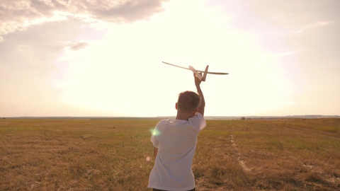 快乐的孩子在田野上的日落背景下带着玩具飞机奔跑。这视频素材模板下载