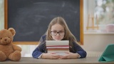 悲伤的十几岁女孩坐在教室里，头靠在书上。不开心高清在线视频素材下载
