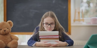 悲伤的十几岁女孩坐在教室里，头靠在书上。不开心