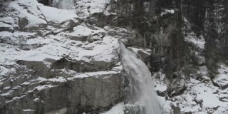 在被雪覆盖的森林中拍摄的小瀑布的4K视频