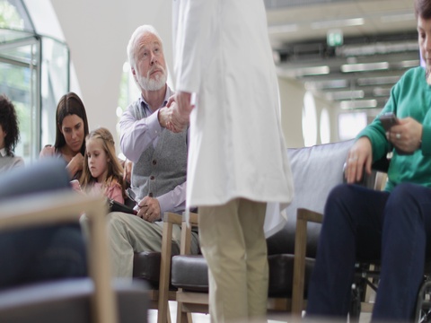 一位年长男士在拥挤的医院等候室里与医生交谈