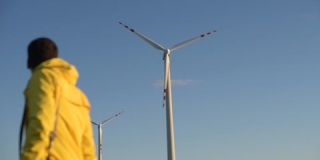 黄色衣服的男人在焦点风力涡轮机的背景上模糊不清