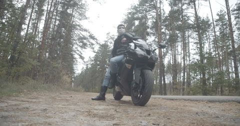 戴着Covid面罩的年轻摩托车手站在黑色摩托车前的宽镜头