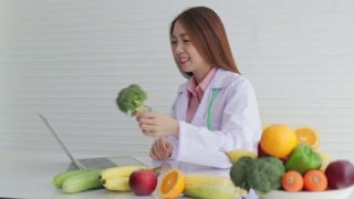美丽的亚洲营养师坐在白色桌子上，周围摆满了各种水果视频素材模板下载
