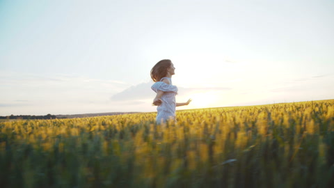 美丽的女孩在阳光照耀的麦田上奔跑