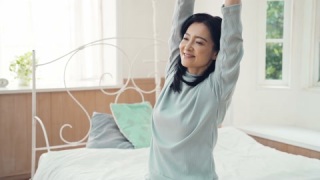 中年亚洲女性在卧室中醒来伸展身体视频素材模板下载