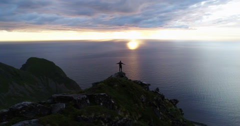 攀登者在山顶上的剪影，伴随着海洋地平线的午夜太阳 - 空中视角