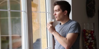 英俊的深色头发男子一边喝着玻璃杯中的咖啡，一边望着窗外