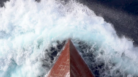 一艘船在海上航行，船首形成海浪溅起，从空中拍摄