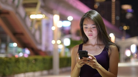 夜晚美丽的亚洲女子在户外使用手机