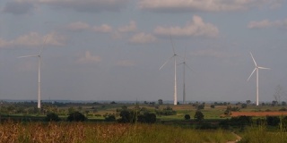 风力涡轮机屹立在农田上方，农民在种植庄稼和照料作物