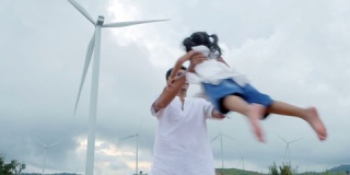 亚洲家庭在风力涡轮机背景下玩耍的场地上玩得很开心