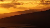 在群山和海洋的背景下，夕阳照亮了风力涡轮机高清在线视频素材下载