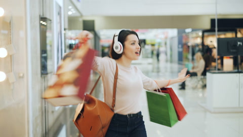 带耳机少女手拎购物袋在购物中心跳舞