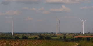 风力涡轮机高耸在农田上，农民在种植作物并照料