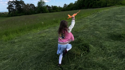 小女孩拿玩具飞机在草地上奔跑视频素材模板下载