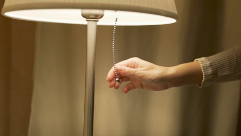一个女人手的特写，包括一盏灯。在舒适的卧室里打开灯