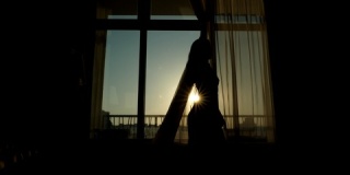 苗条的年轻女子在阳光明媚的早晨，拉开透明的窗帘打开窗户