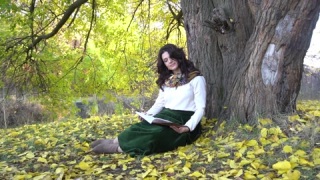 美丽的女人坐在公园落叶上看书。 视频素材模板下载