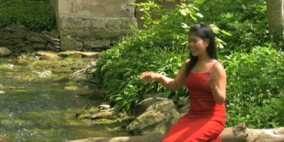 春天，穿着红色连衣裙的亚洲女人坐在河边