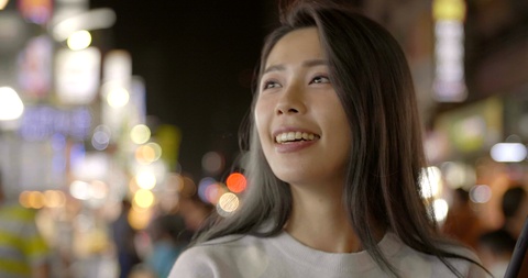 快乐的年轻亚洲女性在夜市使用智能手机