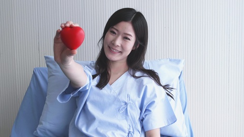 躺在医院的病床妇女表现出手中红色的心