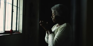 一个精神上的年轻非洲女人站在窗户旁向上帝祈祷