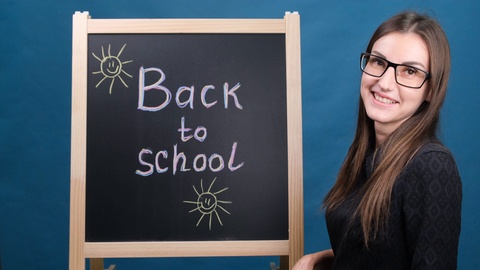 回到学校，一位戴眼镜的女老师站在学校黑板旁边视频素材模板下载
