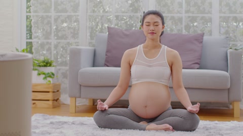 快乐冷静的孕妇深呼吸新鲜空气并做瑜伽莲花坐姿舒适