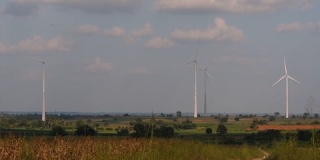风力发电机耸立在农田上方，农民们在种植庄稼和照料作物