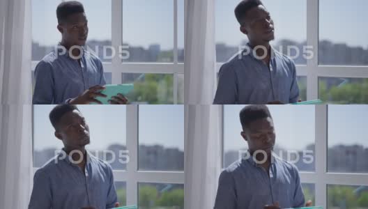 非洲裔美国人站在窗前用平板电脑思考的肖像高清在线视频素材下载