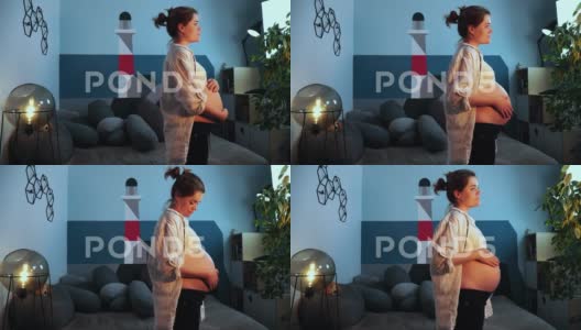 怀孕的女人站在客厅里抚摸她的肚子高清在线视频素材下载
