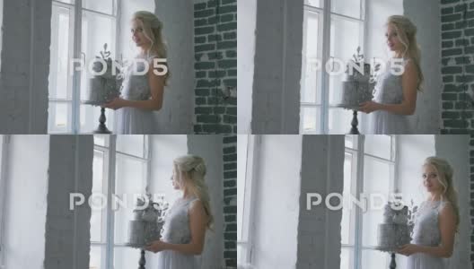 新娘站在窗前，手上拿着一份美丽的婚礼蛋糕高清在线视频素材下载