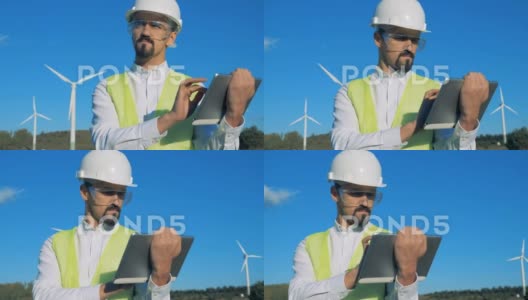 工人站在白色风力涡轮机旁边，在平板电脑上打字。风车，绿色高清在线视频素材下载