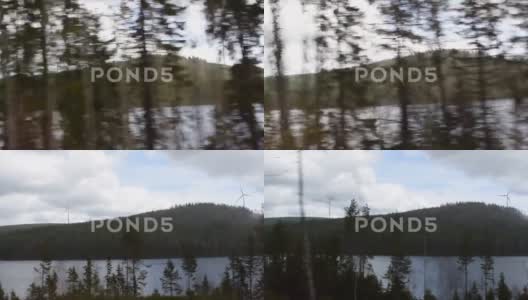 通过驾驶汽车的侧窗看到湖上树木繁茂的山上的风力涡轮机高清在线视频素材下载